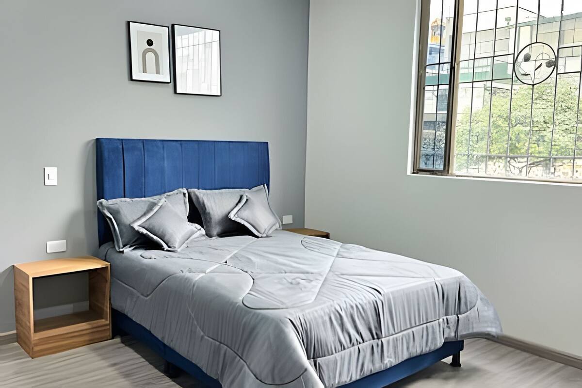 Une chambre à coucher avec un lit, deux tables de chevet, une fenêtre donnant sur un beau paysage et deux tableaux encadrés accrochés au mur.