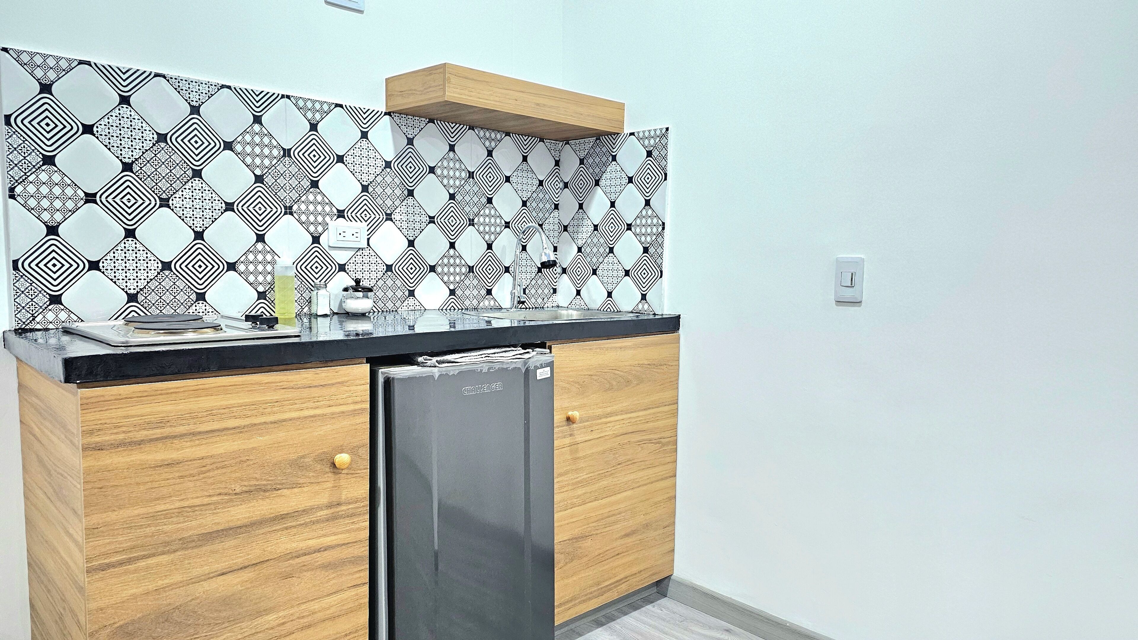 A compact kitchen with a patterned backsplash, a built-in refrigerator, and wooden cabinetry.