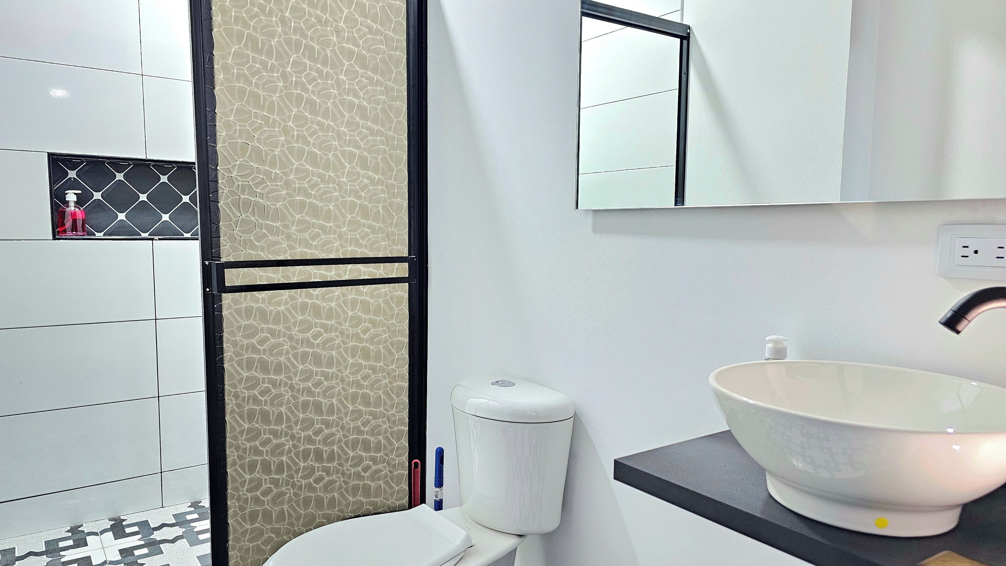 Ein modernes Badezimmer mit Toilette in Weiß, einer strukturierten Wand in Beige, einem Spiegel mit schwarzem Rahmen und einem Waschbecken in Weiß mit Beige-Becken.