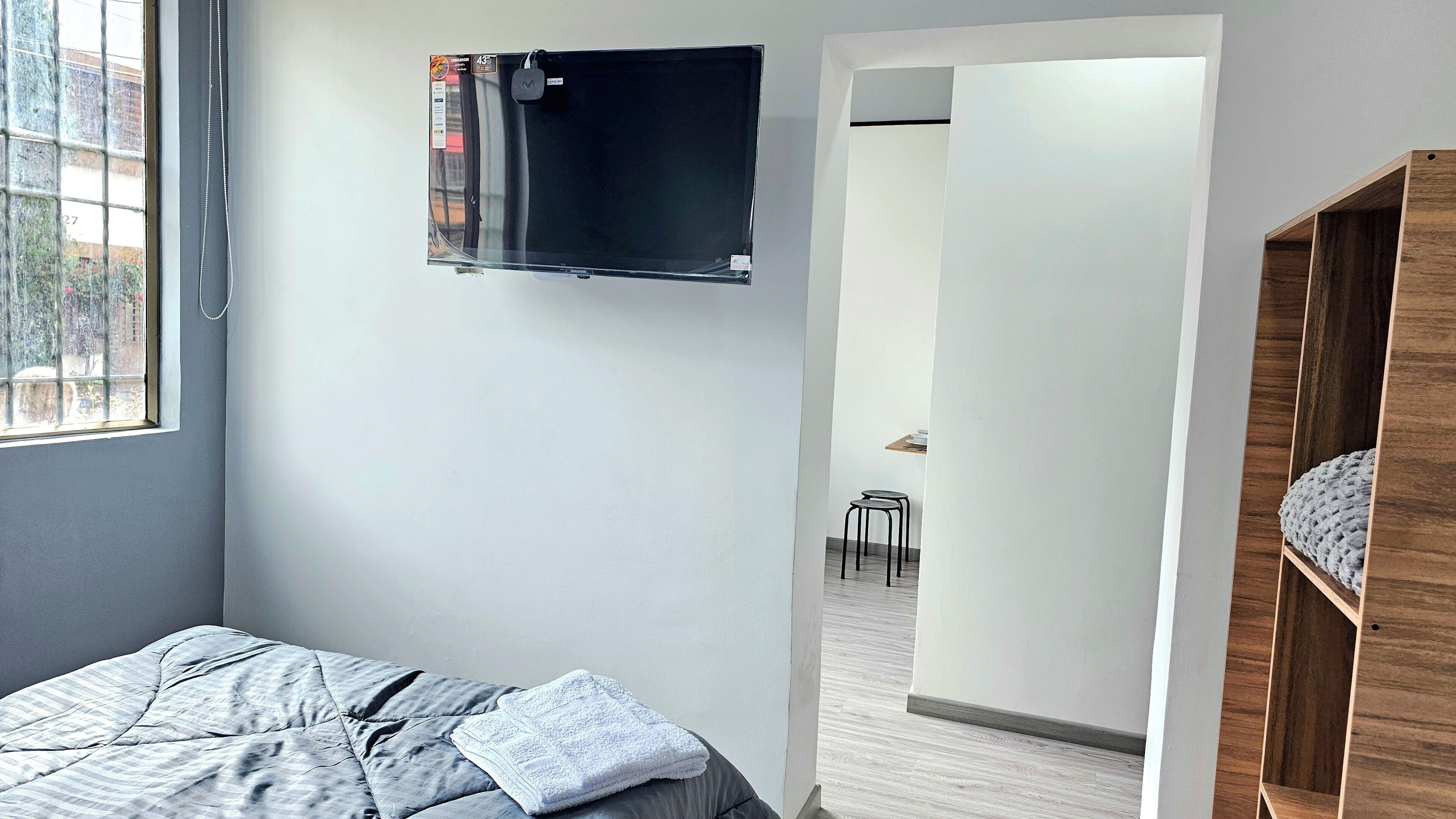 Ein Schlafzimmer mit einem Bett, einem an der Wand montierten Fernseher und einer Holzregaleinrichtung.