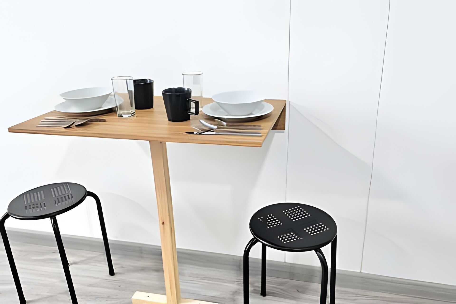Et minimalistisk spisebord med to sorte stole, en træbordplade og en hvid væg i baggrunden.