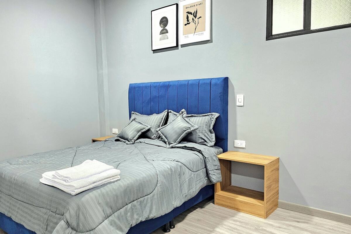 Une chambre à coucher avec un lit, une table de chevet et une étagère fixée au mur.