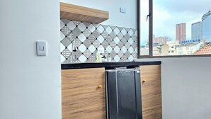 A compact kitchen with a black countertop, wooden cabinets, and a patterned backsplash. A window reveals a cityscape view. - Hotel Ktaleya Apartamentos (Bogotá)
