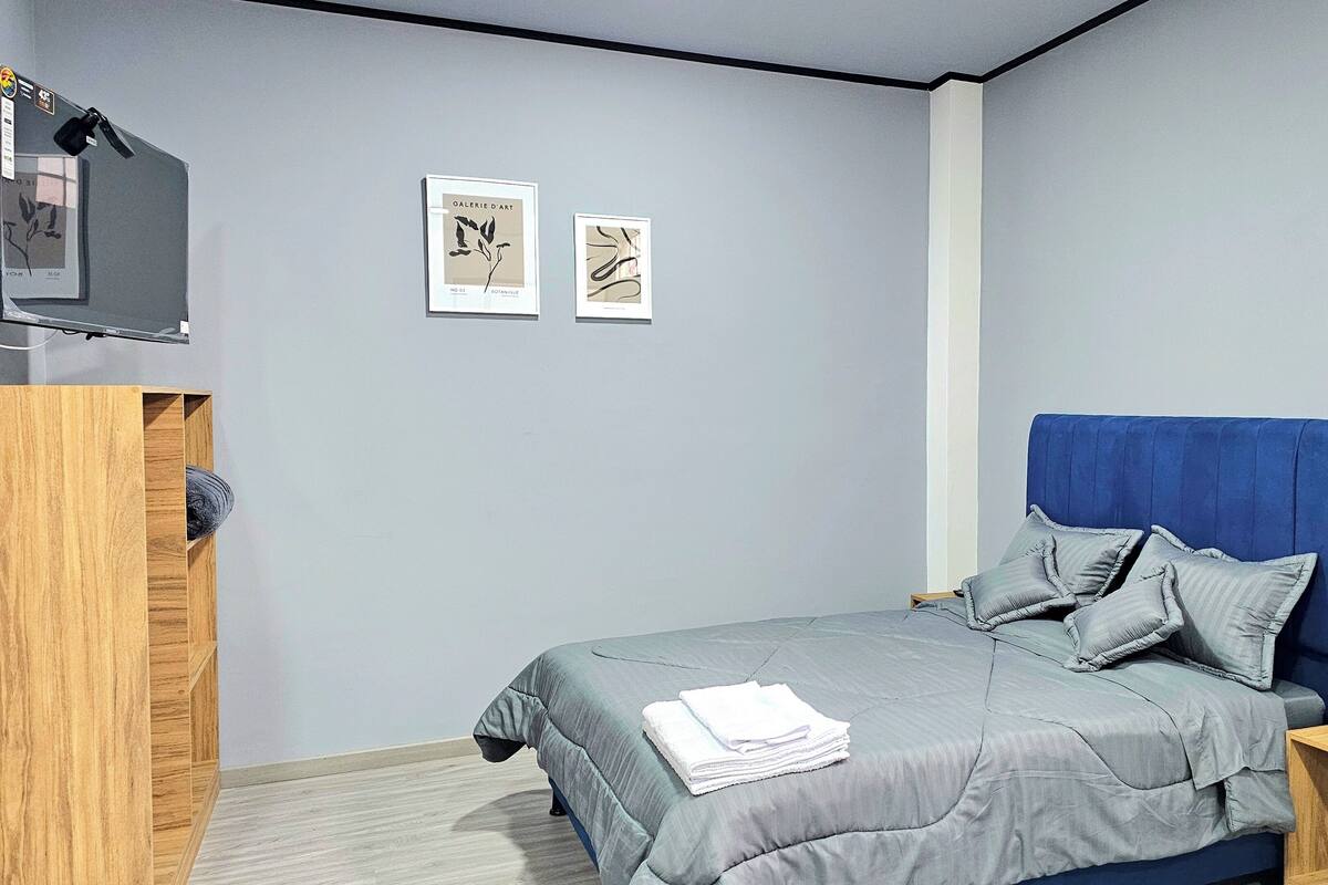 Une chambre à coucher avec un lit, une armoire en bois et deux œuvres d’art encadrées accrochées au mur.