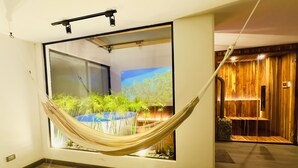 Une pièce avec un hamac, une grande fenêtre donnant sur une forêt et un mur en bois.