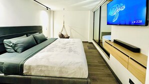 Une chambre d’hôtel moderne avec un grand lit, un téléviseur fixé au mur et un fauteuil suspendu.