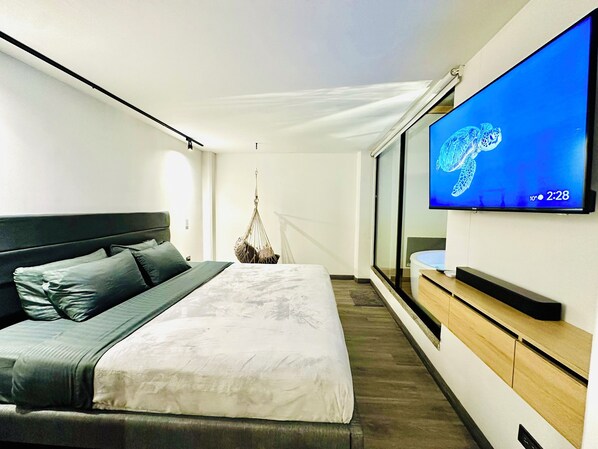 A modern hotel room with a large bed, a TV on the wall, and a hanging chair.