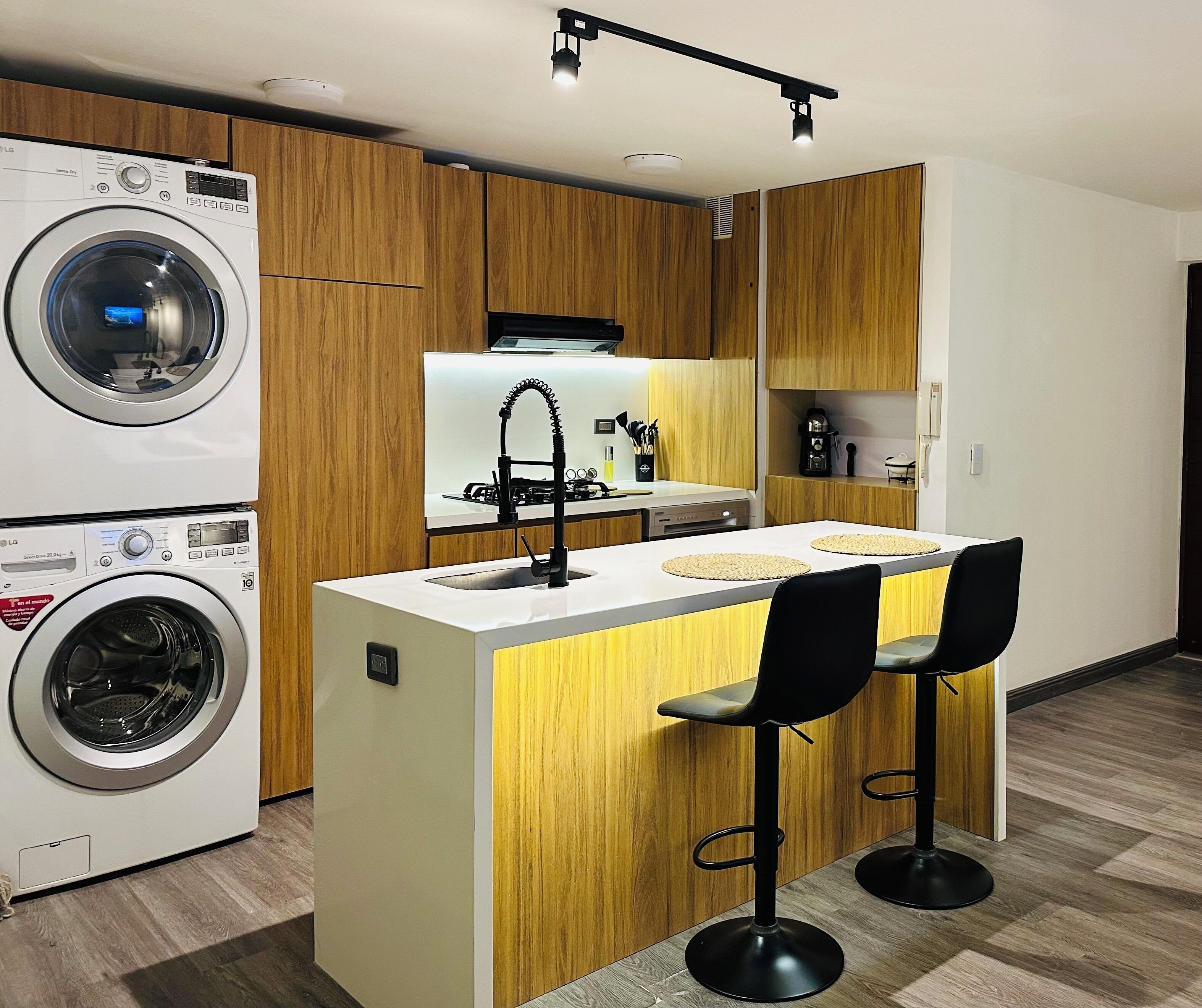 Een moderne keuken met twee LG wasmachines, een centraal eiland met barstoelen, houten kasten en een inbouwmagnetron.