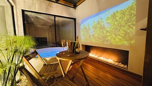 A hot tub with two glasses and a bottle, a wooden deck, and a fireplace with a projected tropical scene. - Apt with private jacuzzi sauna sauna fireplace cinema and gym king size bed 93 park (Bogotá)