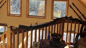 A cozy attic room with wooden beams, a ceiling fan, and three windows offering a view of snow-covered trees. - Cozy 4-bedroom cabin with views of Saddleback mountain- WiFi plus an EV charger (Dallas Plantation)