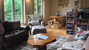 A cozy living room with a fireplace, large windows, a bookshelf, and a dining area. - Cozy 4-bedroom cabin with views of Saddleback mountain- WiFi plus an EV charger (Dallas Plantation)