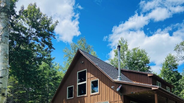 A wooden cabin with a deck, surrounded by a grassy yard and colorful Adirondack chairs. - Cozy 4-bedroom cabin with views of Saddleback mountain- WiFi plus an EV charger (Dallas Plantation)
