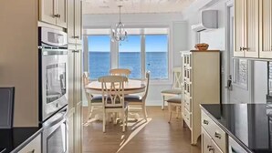 A kitchen with wooden cabinets, a dining table with chairs, and a view of the sea through large windows.