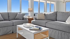 A modern living room with a large gray sectional sofa, a white coffee table, and a wicker side table.