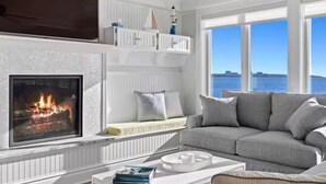 A living room with a fireplace, a sofa, and a view of the ocean.