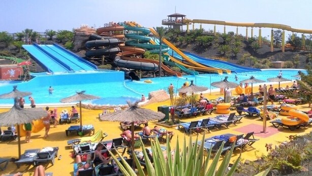 Un parque acuático con varias toboganes y una zona de piscina con tumbonas y sombrillas.