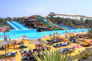 Un parc aquatique doté de nombreux toboggans et d’un espace piscine avec des chaises longues et des parasols.
