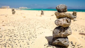 Una pila de rocas sobre una playa arenosa, con un cielo azul despejado y el océano al fondo.
