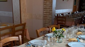 Un espace repas avec des tables dressées pour le repas, comprenant des assiettes blanches, des verres transparents et des petits pains.