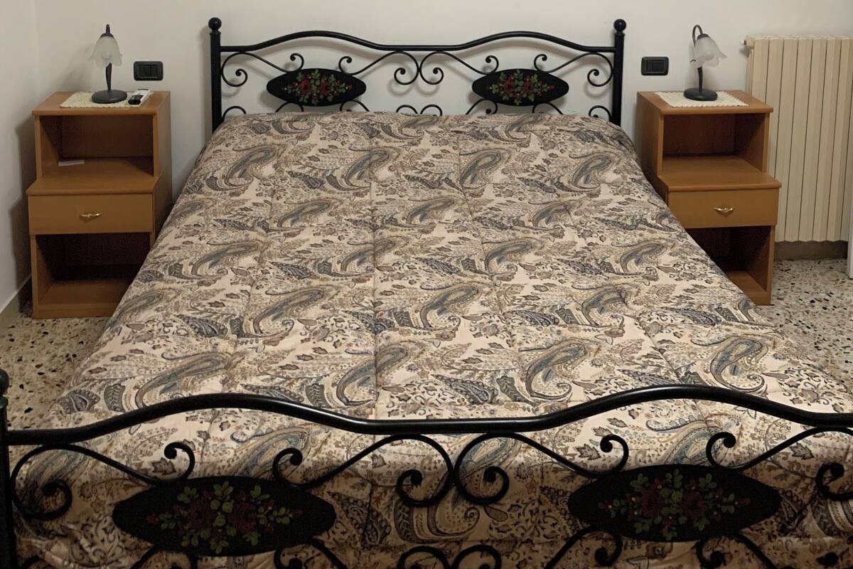Una camera da letto con un letto, due comodini, un condizionatore d'aria a parete e un quadro con fiori.