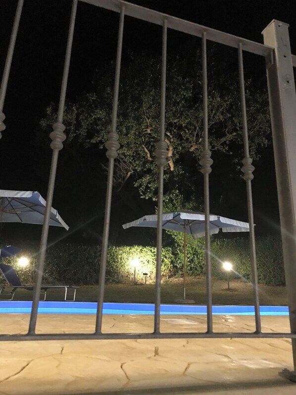 A nighttime outdoor area with a pool, umbrellas, and a metal pergola structure. - agriturismo cerquatonda (Montalto delle Marche)