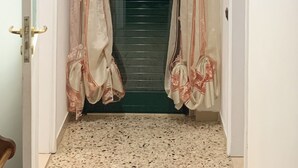 Un couloir étroit orné de rideaux à motifs, une porte avec une poignée dorée et un tableau encadré accroché au mur.