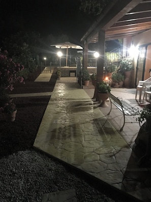 A nighttime outdoor area with a paved walkway, potted plants, and a covered seating area. - agriturismo cerquatonda (Montalto delle Marche)