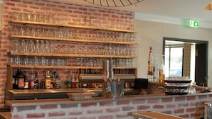 A bar area with a brick wall, shelves with glasses, and bottles.