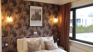 A hotel room with a bed, a framed picture of a building, and a window with curtains.