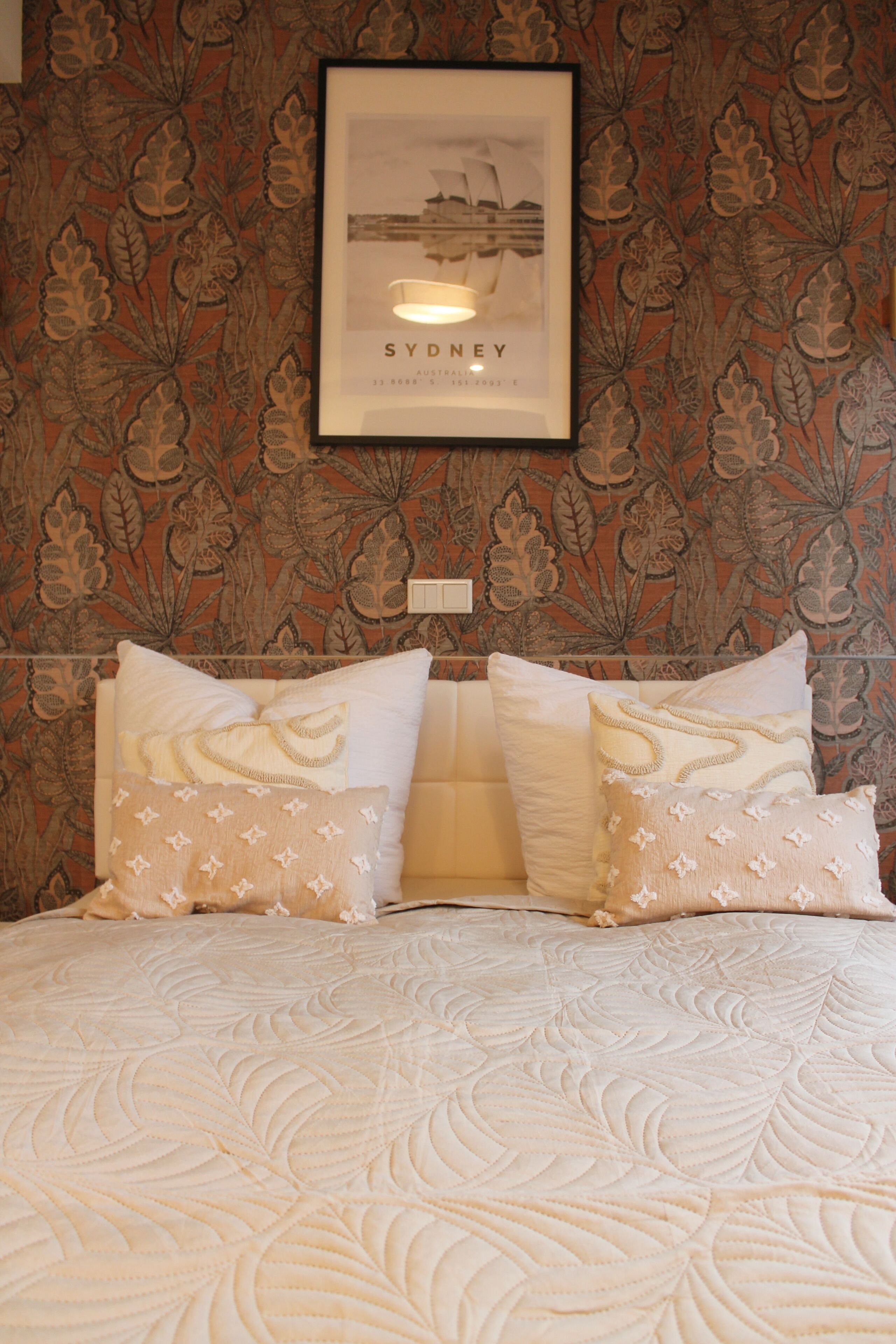 A bed with a floral-patterned headboard, a framed picture above it, and two decorative pillows.