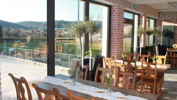 A dining area with a view of the countryside, wooden furniture, and potted plants.