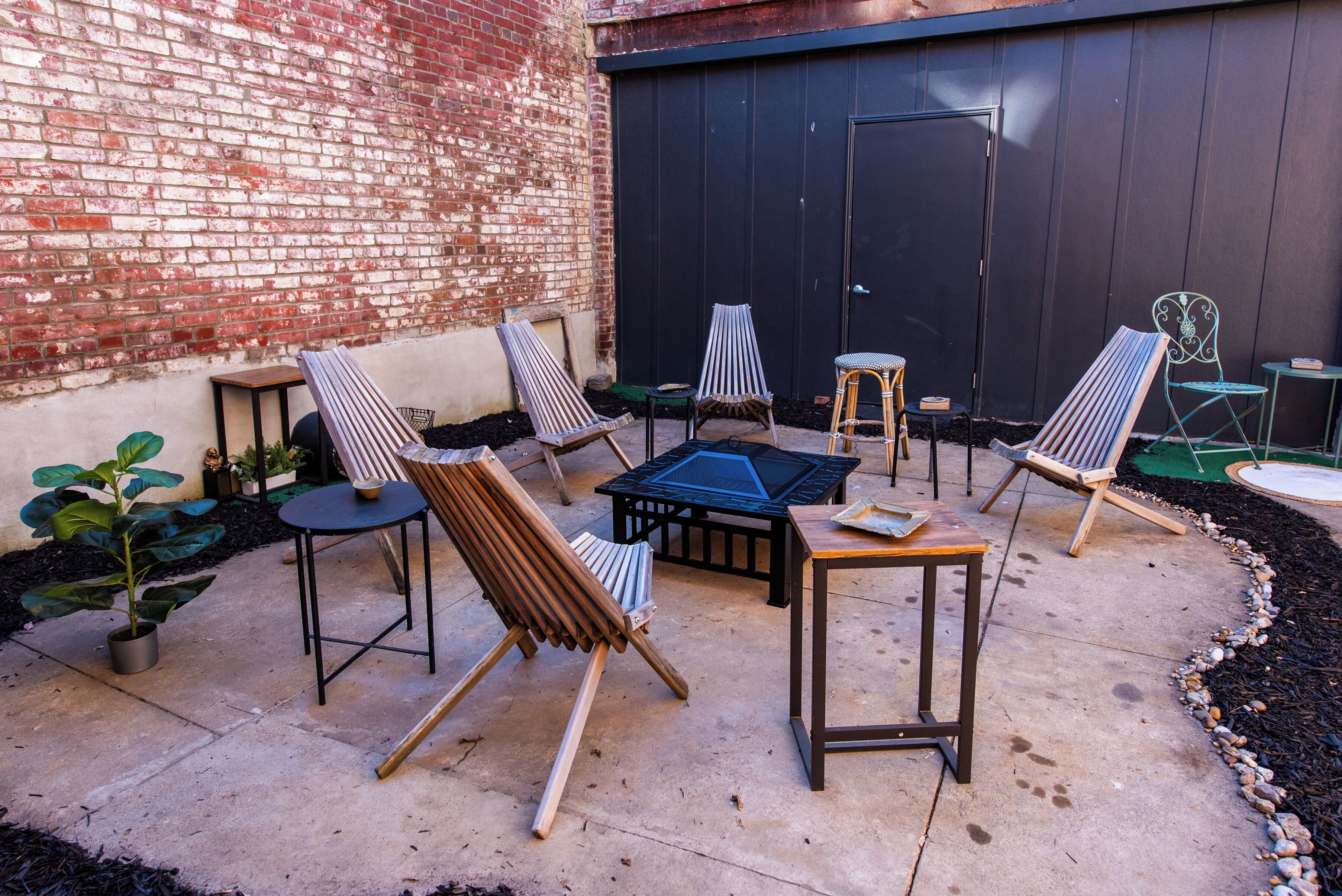 An outdoor patio with several lounge chairs and a small table, surrounded by a brick wall and a dark fence.
