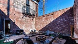 Un patio de ladrillo con mobiliario exterior, una parrilla y una mesita.