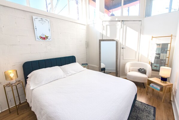 Habitación de hotel con una cama grande, una silla, una mesita con lámpara, un espejo y un certificado enmarcado en la pared.
