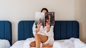 A person sitting on a bed with a book titled 'VOICE' and another book titled 'ROLEX'.