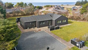 A modern two-story house with a dark exterior, a covered patio, and a view of the sea.