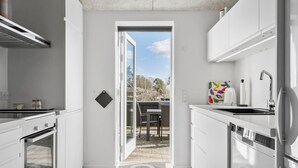 A modern kitchen with white cabinetry, a built-in oven, and a dishwasher. There is a small dining area with a table and chairs visible through an open door.