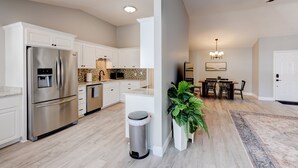 Una cocina moderna con electrodomésticos de acero inoxidable, armarios blancos y un comedor con mesa y sillas de madera.