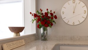 Una encimera de cocina con un jarrón de rosas rojas, un reloj y una placa con la inscripción 'THOMASVILLE'.