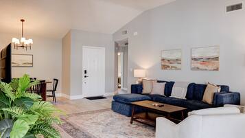 A living room with a sofa, ottoman, coffee table, and a dining area with chairs and a table.