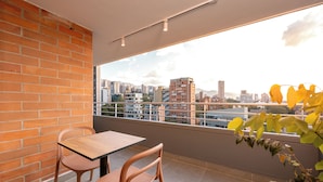 Uma varanda com parede de tijolos, uma mesa, duas cadeiras e vista para a paisagem urbana.