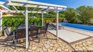 Un área de piscina al aire libre con una pérgola, suelo de piedra y sillones de descanso.