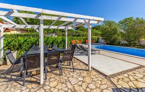 Un área de piscina al aire libre con una pérgola, suelo de piedra y sillones de descanso.