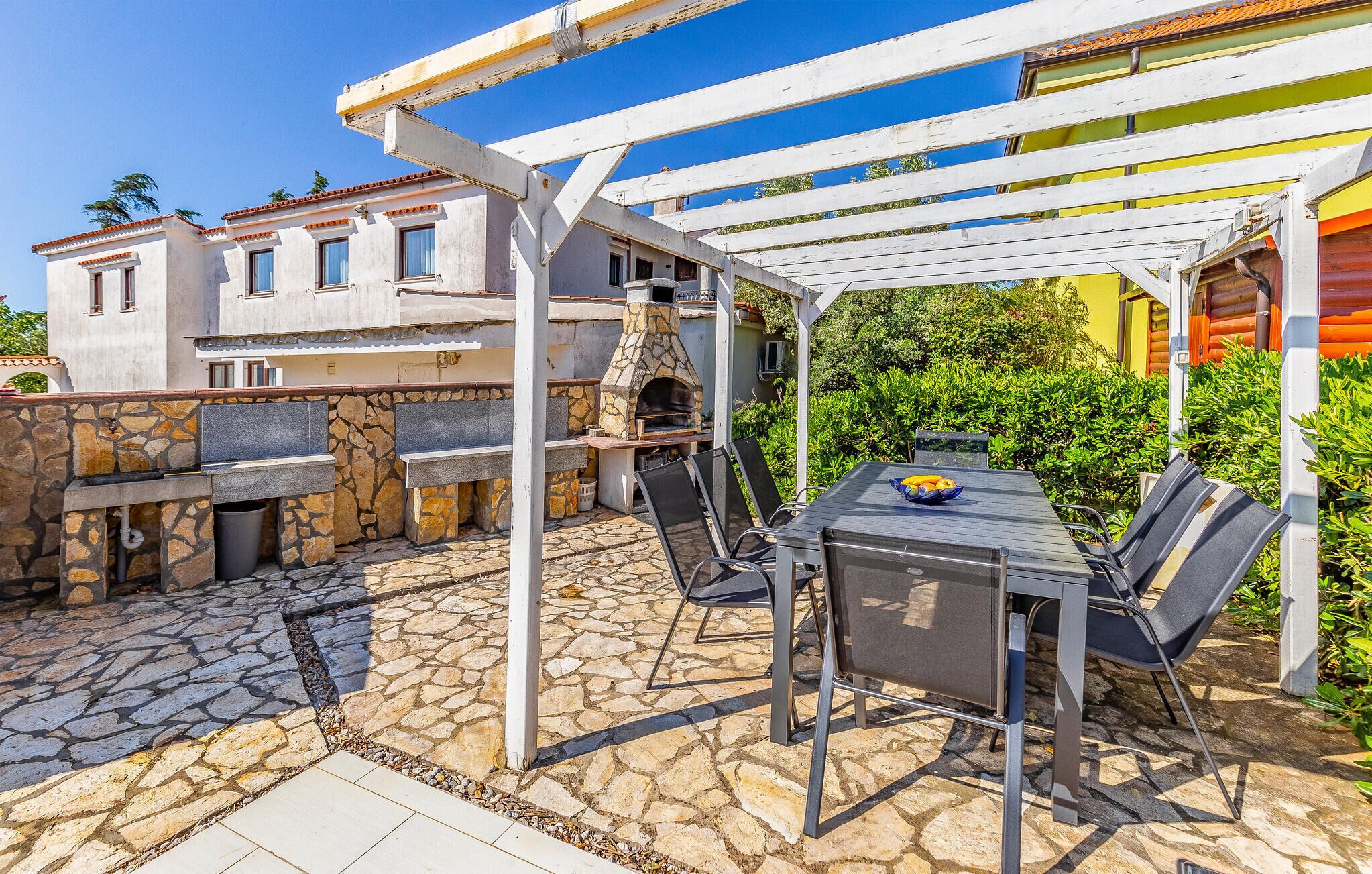 Un patio al aire libre con suelo de piedra, una parrilla y una mesa con sillas.