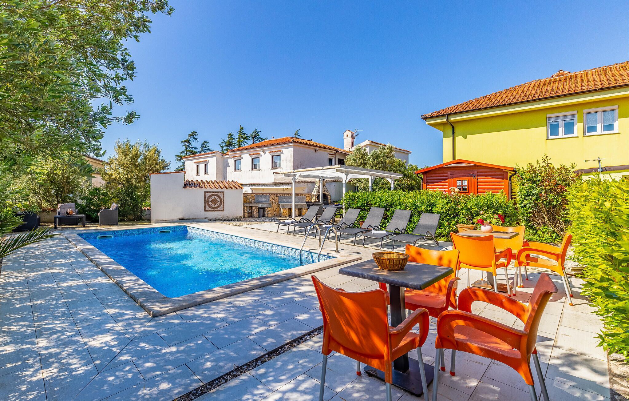 A swimming pool with lounge chairs and a table, surrounded by greenery and buildings.