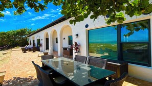 A patio with a glass table and wicker chairs, surrounded by white walls with arches and large windows. - Ocean front Luxury Hacienda with pool,  pet friendly 5 (Cocoa Beach)