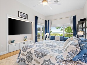 A bedroom with a large bed, a flat-screen TV, a window with curtains, and a view of the outdoors. - Ocean front Luxury Hacienda with pool,  pet friendly 5 (Cocoa Beach)