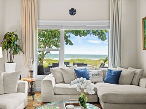 A living room with a view of the beach, a sofa with decorative pillows, a potted plant, and a glass coffee table. - Ocean front Luxury Hacienda with pool,  pet friendly 5 (Cocoa Beach)