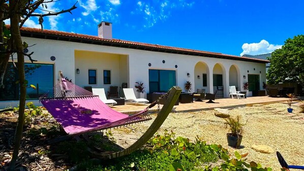 A white building with a tiled roof, outdoor seating area with white chairs, and a hammock. - Ocean front Luxury Hacienda with pool,  pet friendly 5 (Cocoa Beach)