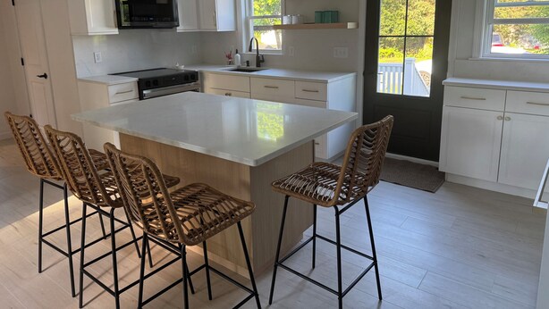 Una cocina moderna con armarios blancos, una isla central y taburetes de bar.